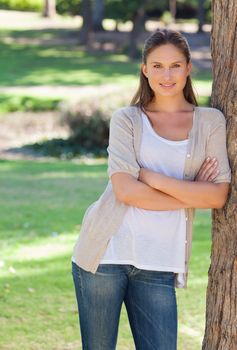 Smiling young woman with her arms crossed leaning against a tree