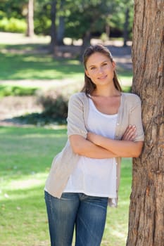 Smiling young woman with her arms folded leaning against a tree