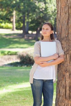 Young woman with a laptop leaning against a tree