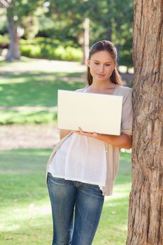 Young woman using a laptop while leaning against a tree