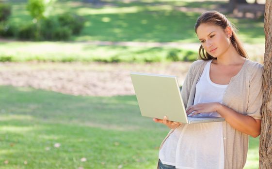 Young woman leaning against a tree while using a laptop