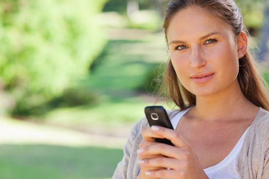Close up of young woman holding her mobile phone in the park