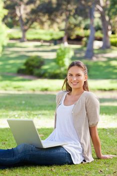 Smiling young woman with her laptop sitting in the park