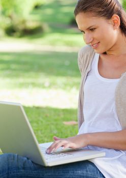 Smiling young woman using her laptop while sitting on the lawn