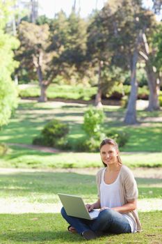 Smiling young woman sitting on the lawn with her laptop