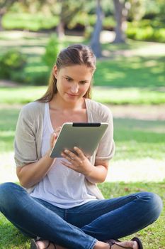 Young woman sitting on the grass while using her tablet computer