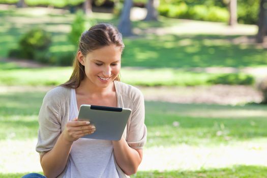 Smiling young woman with her tablet computer sitting on the lawn