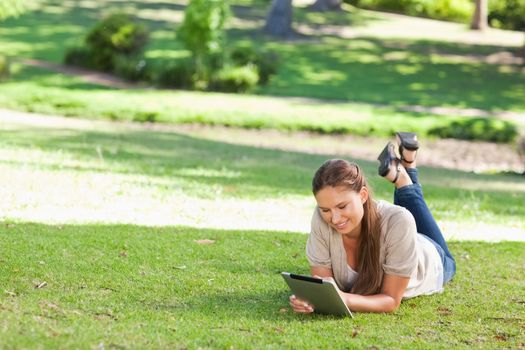 Smiling young woman lying on the lawn with a tablet computer