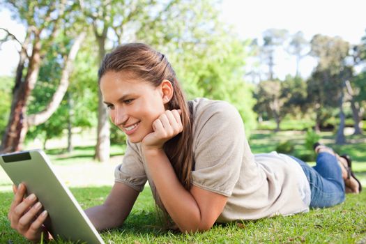 Smiling young woman laying on the lawn with her tablet computer