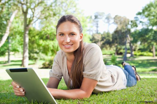 Smiling young woman with her tablet computer lying on the lawn