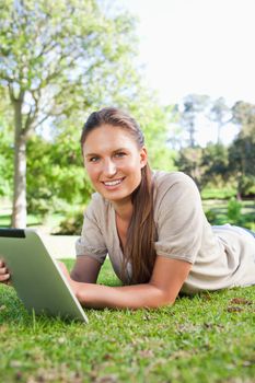 Smiling young woman lying on the grass with her tablet computer