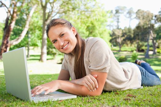 Smiling young woman lying on the lawn with her laptop