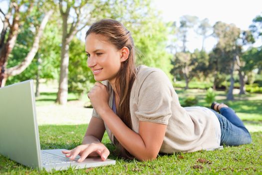 Smiling young woman lying on the lawn with her notebook