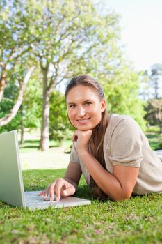 Smiling young woman with her laptop while lying on the lawn