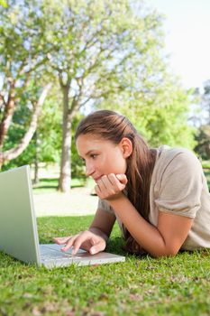 Young woman lying on the lawn while using her laptop