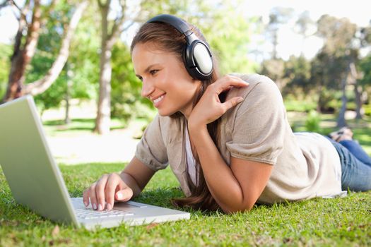 Young woman with a laptop and a headset lying on the lawn