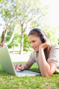 Young woman with headphones and a laptop lying on the lawn