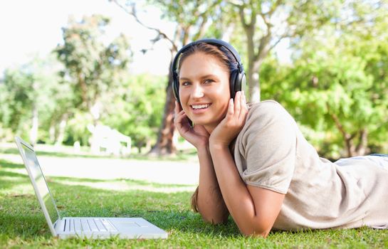 Young woman with a laptop and headphones lying on the lawn