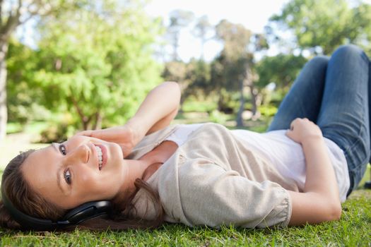 Smiling young woman lying on the lawn while listening to music