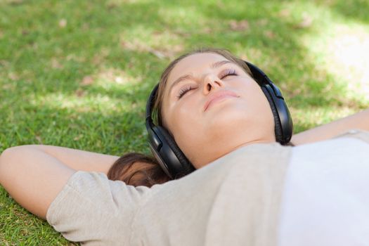 Relaxed young woman lying on the lawn enjoying music