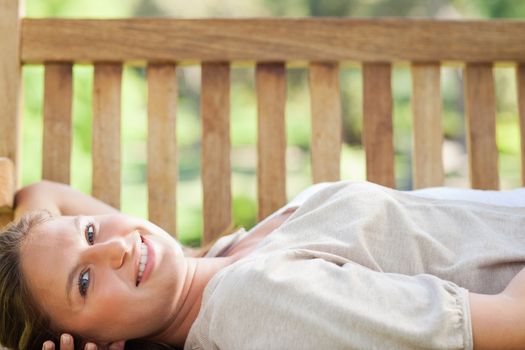 Smiling young woman lying on a park bench