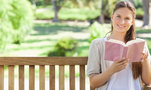 Smiling young woman reading a book on a park bench