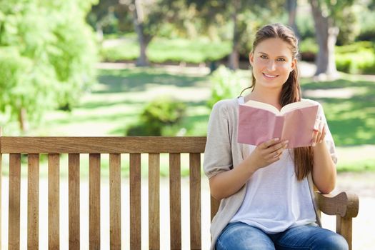 Young woman sitting with a book on a park bench