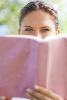 Young woman hiding her face behind a book in the park