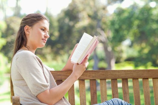Side view of a young woman reading while sitting on a park bench