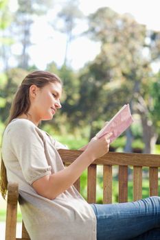 Side view of a young woman reading a book on a park bench