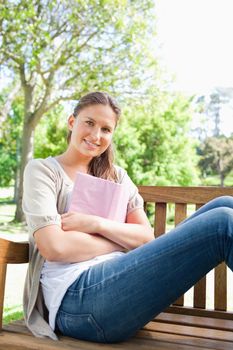 Smiling young woman sitting on a park bench with her book