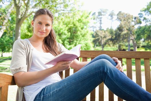 Young woman sitting on a park bench with a book