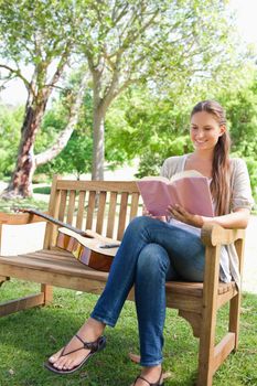 Smiling young woman sitting on a bench with a book and a guitar