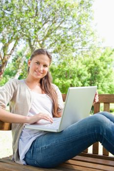 Smiling young woman with a laptop sitting on a park bench