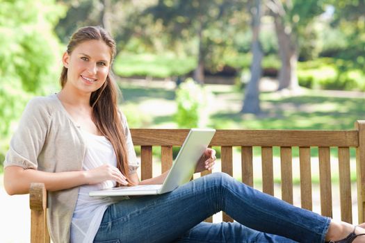 Smiling young woman with her laptop on a park bench