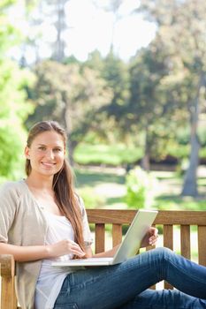Smiling young woman with her notebook on a park bench
