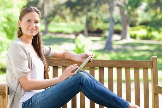 Side view of a smiling young woman using a tablet computer on a park bench