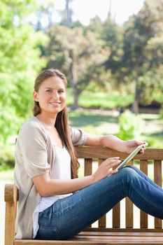 Side view of a smiling young woman with a tablet computer on a park bench