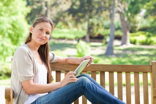 Side view of a young woman with a tablet computer on a park bench