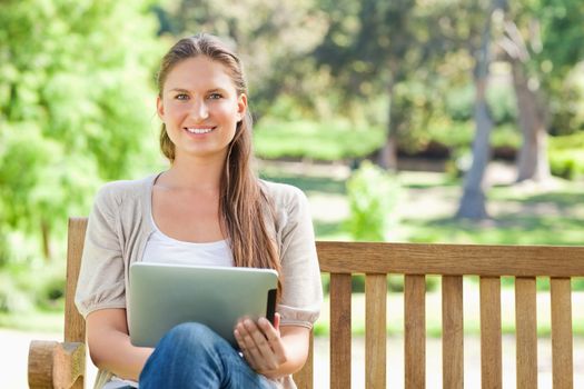 Smiling young woman with a tablet computer on a park bench