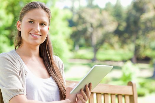 Smiling young woman with a tablet on a park bench