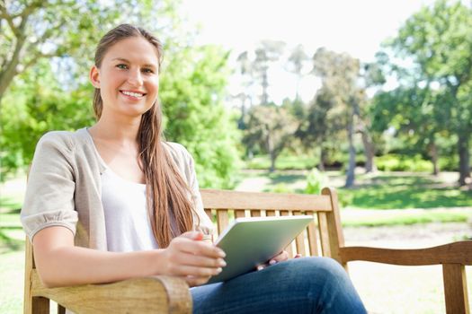 Smiling young woman on a bench in the park with her tablet computer