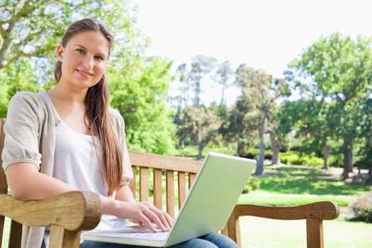 Smiling young woman with a laptop on a park bench