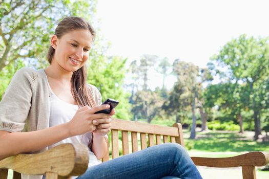 Smiling young woman reading text message on a park bench