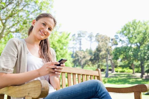 Smiling young woman writing a text message on a park bench