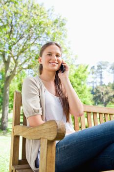 Smiling young woman on her phone on a park bench