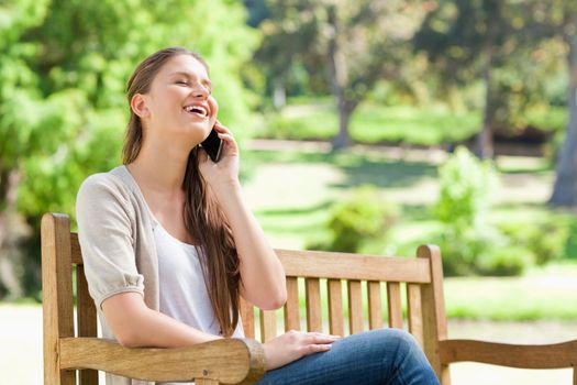 Laughing young woman on her cellphone on a park bench