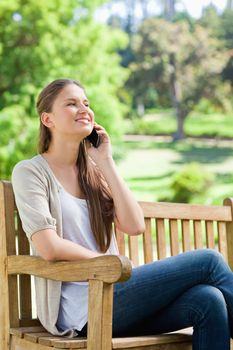 Smiling young woman sitting with her cellphone on a park bench