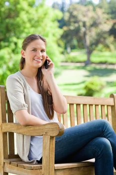 Smiling young woman sitting with her mobile phone on a park bench