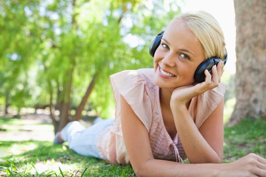 Smiling young woman lying on the lawn while wearing headphones